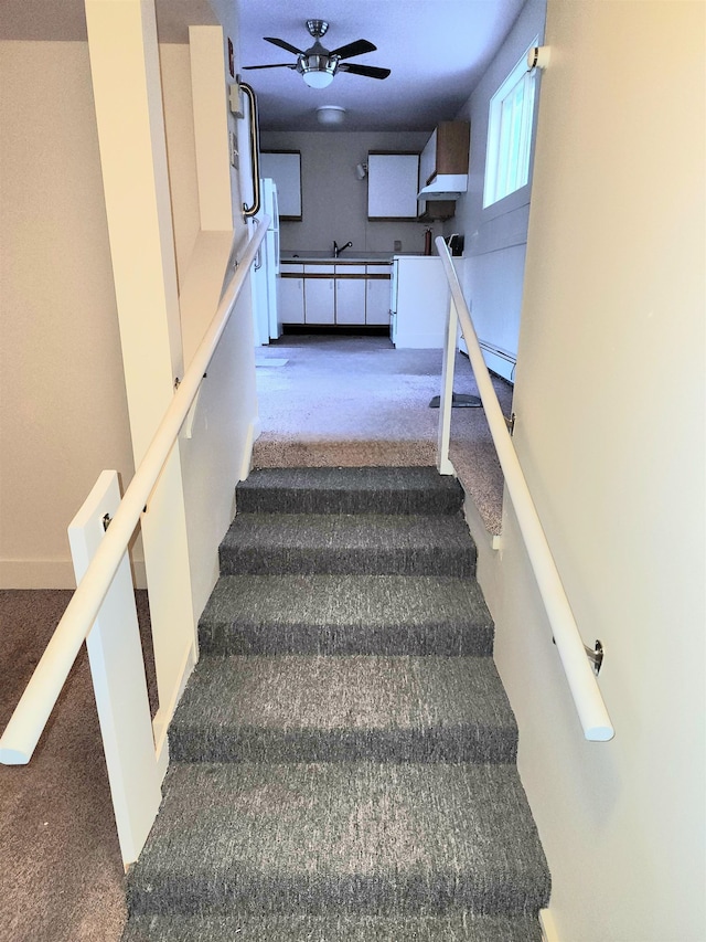 stairway with carpet, baseboard heating, and ceiling fan