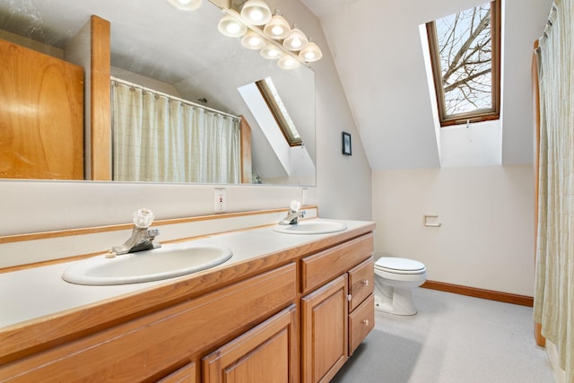 bathroom with vaulted ceiling with skylight, double vanity, a sink, and baseboards