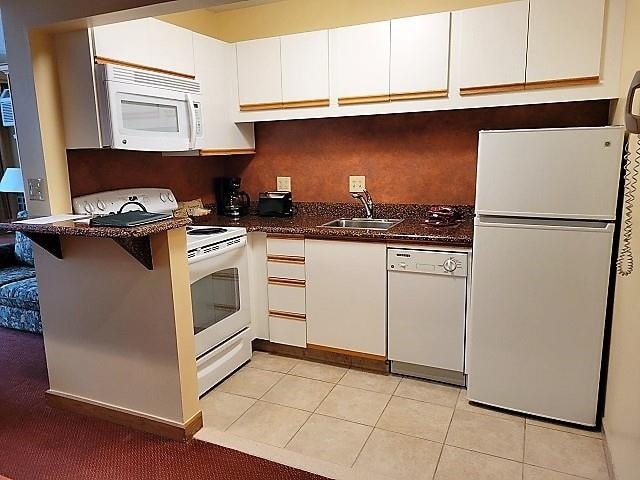 kitchen featuring sink, white appliances, light tile floors, and white cabinets