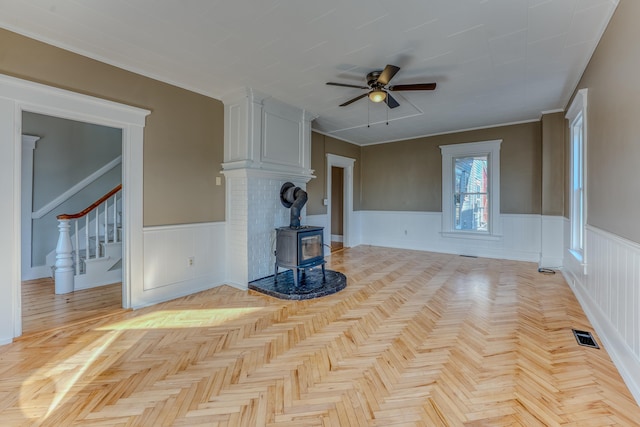 unfurnished living room featuring light parquet floors, a wood stove, and ceiling fan