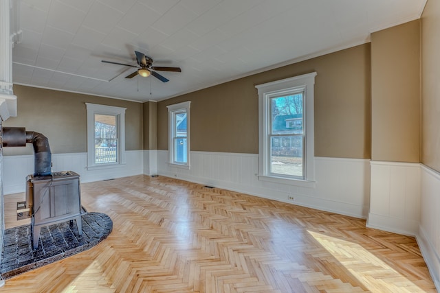 living room featuring ceiling fan, light parquet flooring, a wealth of natural light, and a wood stove