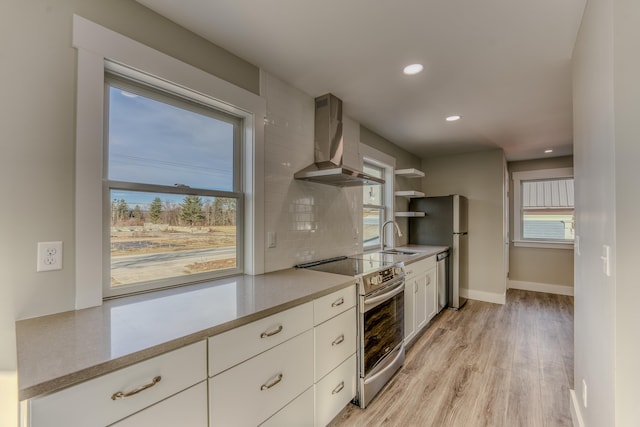 kitchen with appliances with stainless steel finishes, light hardwood / wood-style floors, wall chimney exhaust hood, backsplash, and sink