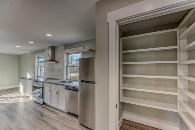 kitchen with stainless steel appliances, light hardwood / wood-style floors, sink, wall chimney exhaust hood, and white cabinets