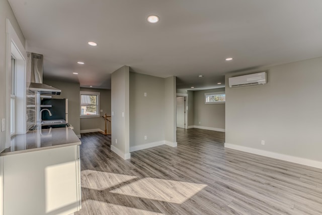 kitchen featuring a wall unit AC, sink, wall chimney exhaust hood, and light hardwood / wood-style floors