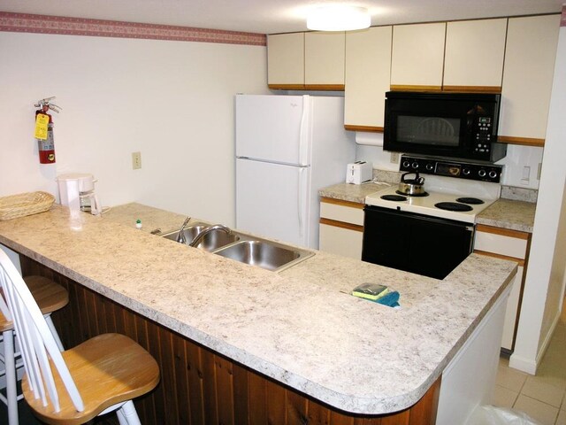 kitchen with a breakfast bar area, white appliances, light tile floors, sink, and cream cabinets