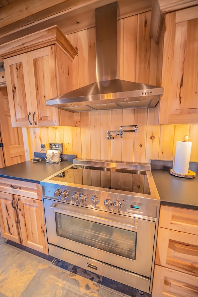 kitchen featuring range with two ovens, light brown cabinetry, tile floors, and wall chimney range hood