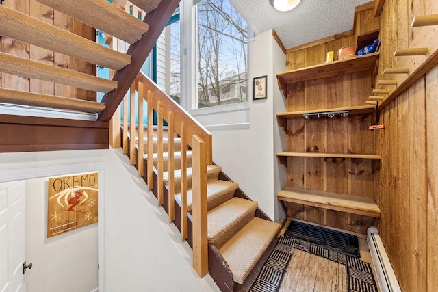 stairs featuring wood walls, a baseboard radiator, and a textured ceiling