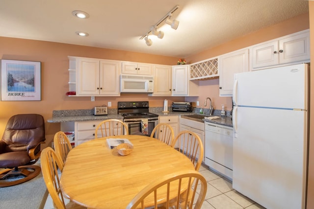 kitchen with white appliances, track lighting, light tile patterned floors, sink, and white cabinetry