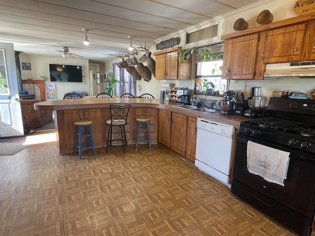 kitchen with black range with gas stovetop, white dishwasher, a sink, under cabinet range hood, and a peninsula