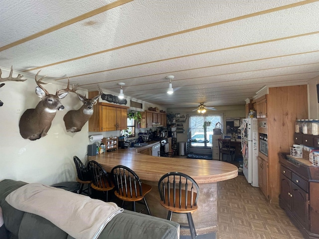 kitchen featuring a textured ceiling, a peninsula, a breakfast bar, freestanding refrigerator, and brown cabinets