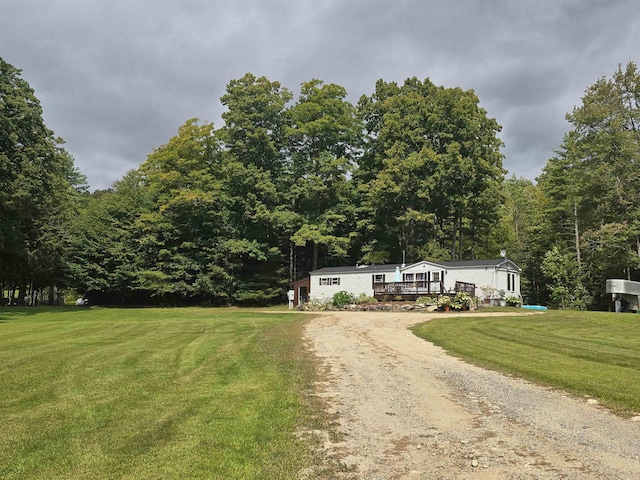 manufactured / mobile home featuring a front lawn, a view of trees, a deck, and dirt driveway