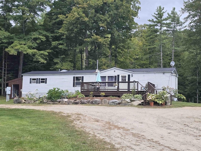 manufactured / mobile home with a front yard, metal roof, a view of trees, driveway, and a wooden deck