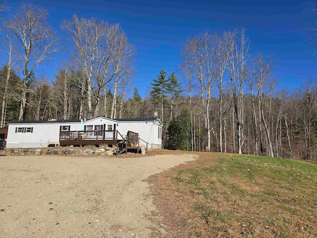 exterior space with driveway, a front yard, a wooded view, and a wooden deck