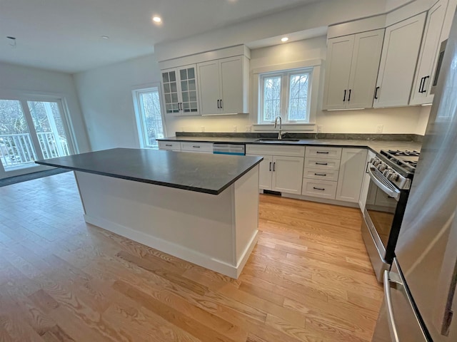 kitchen featuring light wood-type flooring, white cabinets, appliances with stainless steel finishes, sink, and a center island