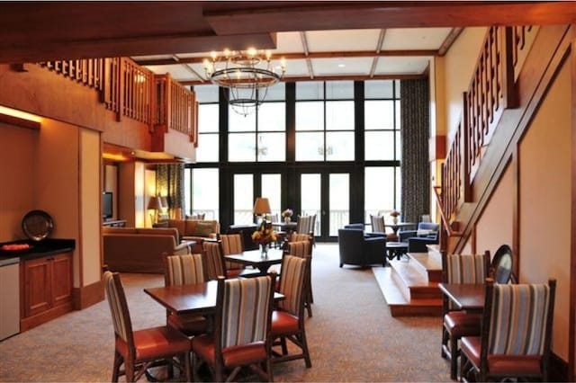 carpeted dining space with an inviting chandelier, beam ceiling, floor to ceiling windows, a towering ceiling, and french doors