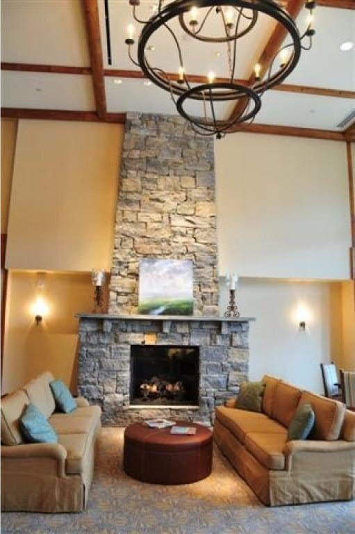 living room featuring beamed ceiling, a stone fireplace, and an inviting chandelier