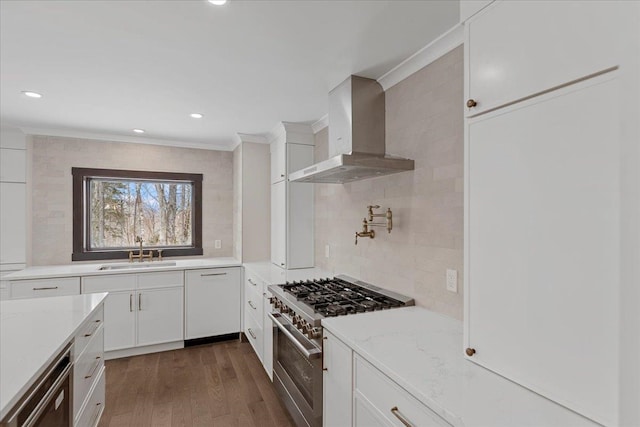 kitchen featuring wall chimney exhaust hood, high end stainless steel range, white dishwasher, sink, and white cabinets