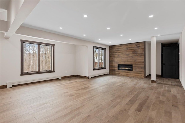 unfurnished living room with light hardwood / wood-style flooring, a baseboard heating unit, and a large fireplace