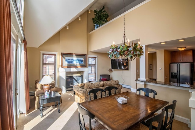 carpeted dining room with a towering ceiling, a baseboard heating unit, and a notable chandelier