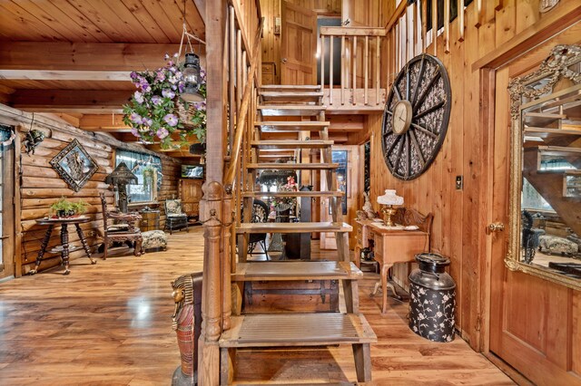 stairway with log walls, light wood-type flooring, wood walls, beam ceiling, and wood ceiling