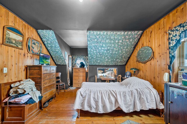 bedroom with lofted ceiling, wood walls, and light hardwood / wood-style flooring