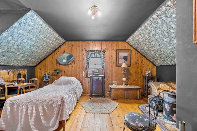 bedroom with wooden walls, light hardwood / wood-style floors, and vaulted ceiling