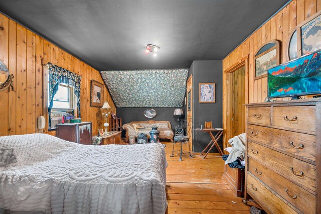 bedroom featuring lofted ceiling, wooden walls, and light hardwood / wood-style flooring