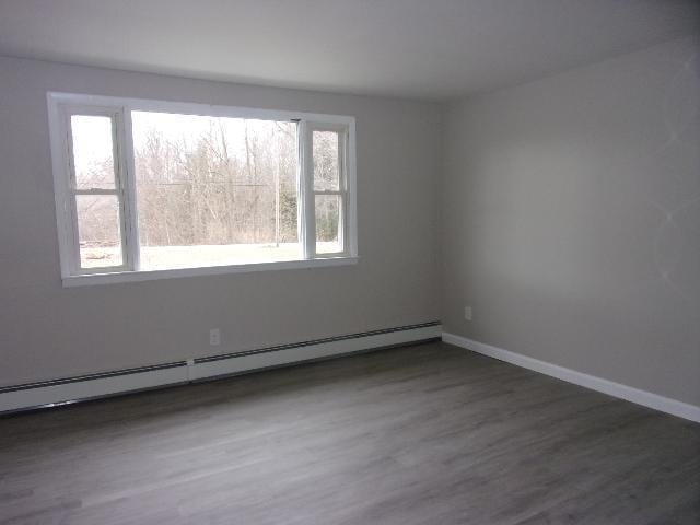 spare room featuring baseboard heating, dark wood-type flooring, and a healthy amount of sunlight