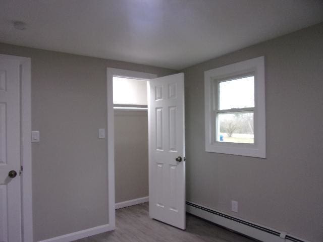 unfurnished bedroom with a closet, a baseboard radiator, and light wood-type flooring