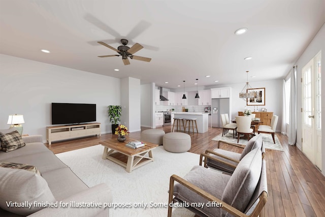 living room featuring ceiling fan with notable chandelier and light hardwood / wood-style flooring