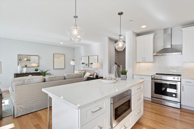 kitchen featuring white cabinets, wall chimney exhaust hood, appliances with stainless steel finishes, and light hardwood / wood-style flooring