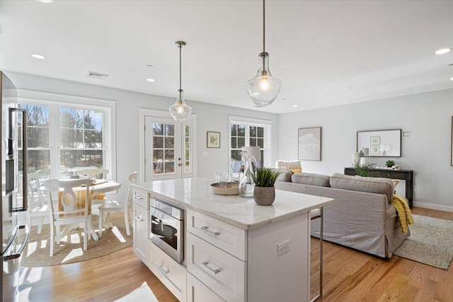 kitchen with light stone countertops, a center island, pendant lighting, white cabinets, and light wood-type flooring