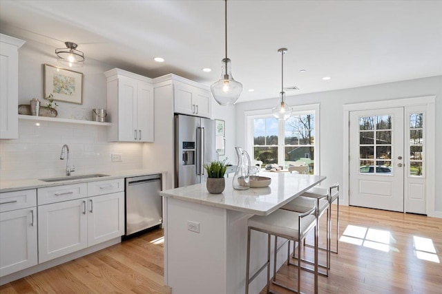 kitchen with sink, light wood-type flooring, an island with sink, appliances with stainless steel finishes, and white cabinetry