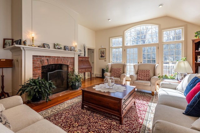 living room featuring hardwood / wood-style flooring, a fireplace, a high ceiling, and a baseboard heating unit