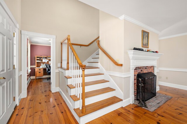 stairway with a fireplace, crown molding, and light wood-type flooring