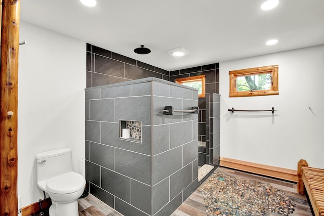 bathroom featuring wood-type flooring, toilet, and a tile shower