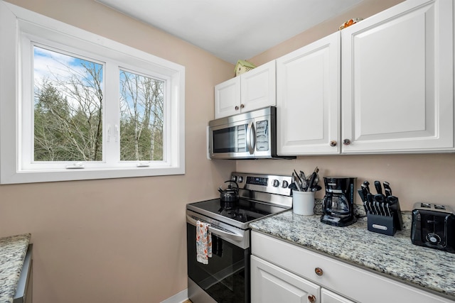 kitchen with stainless steel appliances, white cabinets, and light stone counters