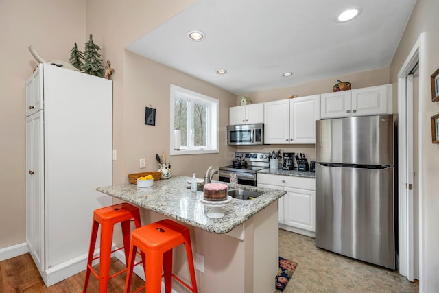 kitchen with appliances with stainless steel finishes, white cabinets, a breakfast bar area, light hardwood / wood-style flooring, and light stone countertops