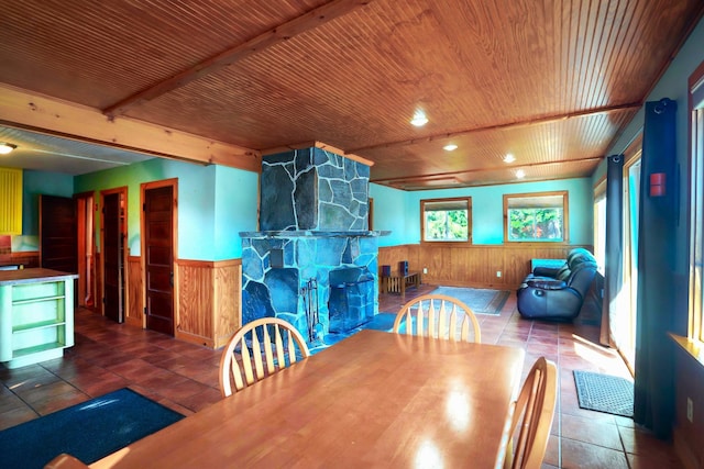 dining area featuring a wainscoted wall, a stone fireplace, wooden ceiling, and tile patterned flooring