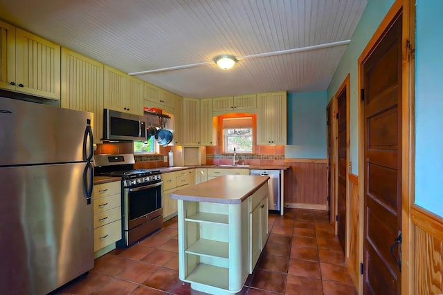 kitchen with open shelves, stainless steel appliances, cream cabinets, and wainscoting