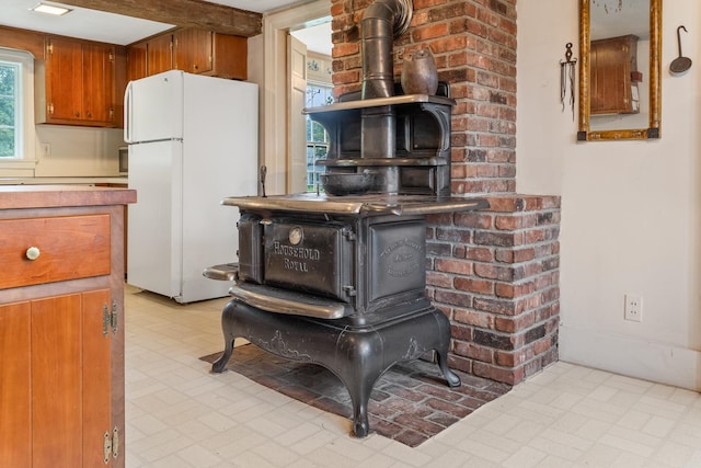 interior details with white fridge, a wood stove, light tile flooring, and beam ceiling