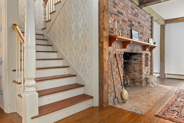 stairs with a brick fireplace, beamed ceiling, and hardwood / wood-style floors