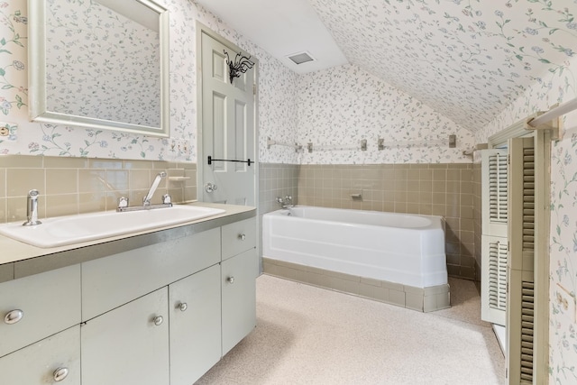 bathroom featuring vanity with extensive cabinet space, tile walls, a bathing tub, vaulted ceiling, and a textured ceiling