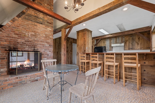 unfurnished dining area featuring carpet floors, a fireplace, vaulted ceiling with beams, brick wall, and an inviting chandelier