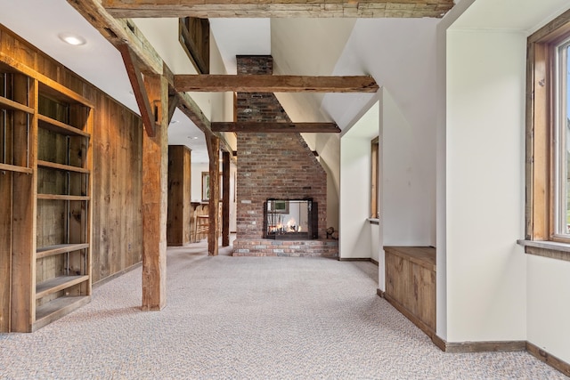 unfurnished living room with wooden walls, carpet floors, a brick fireplace, brick wall, and beam ceiling