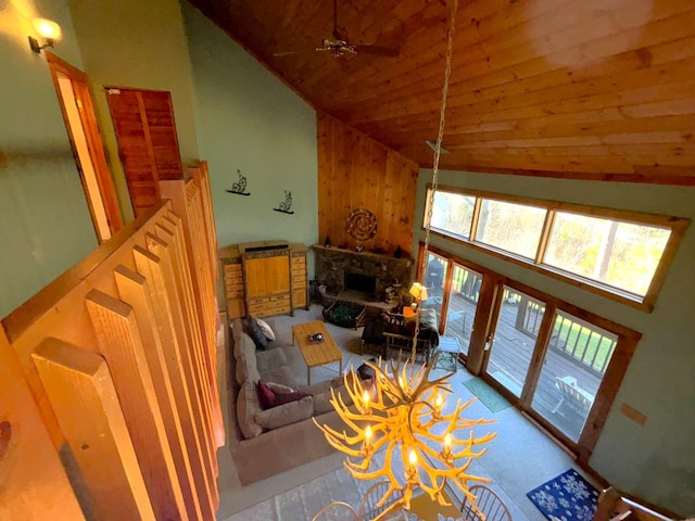 living room featuring a stone fireplace, high vaulted ceiling, wooden ceiling, and ceiling fan with notable chandelier