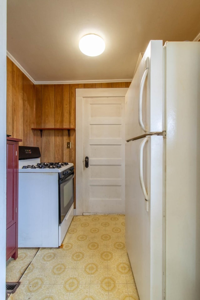 kitchen featuring white refrigerator, ornamental molding, wooden walls, and range with gas stovetop