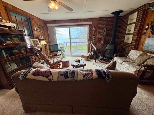 living room featuring a wood stove, wood walls, carpet flooring, and ceiling fan