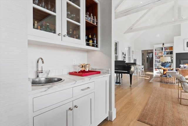 bar featuring a sink, beam ceiling, light wood-type flooring, high vaulted ceiling, and decorative backsplash