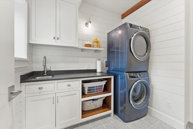 washroom with stacked washer / dryer, a sink, wooden walls, tile patterned floors, and cabinet space